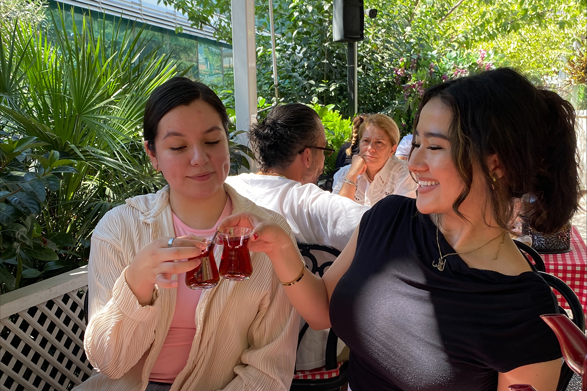 Two young women clink their tea glasses together